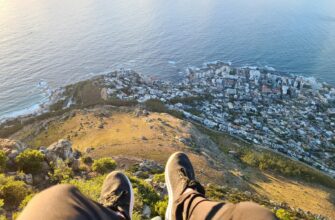 person in brown pants and black shoes sitting on brown rock near body of water during