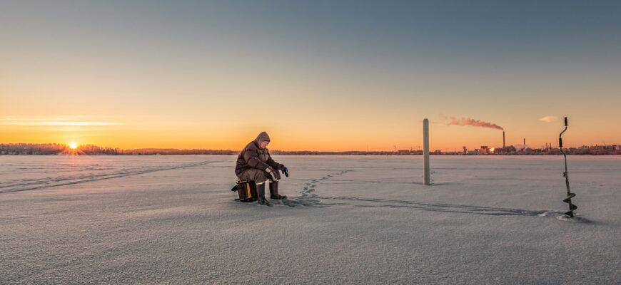 person sitting on stool on ice field near manual auger